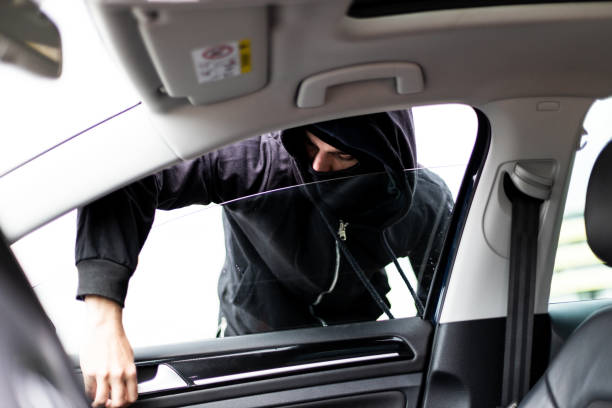 istock Hooded thief with mask stealing from a parked car 1311992965