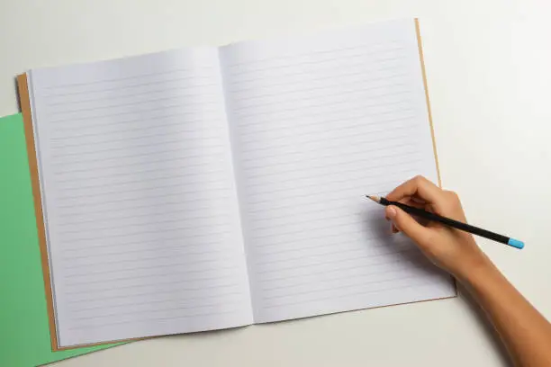 Photo of Kid hand with pencil and open notebook on white background. Top view.