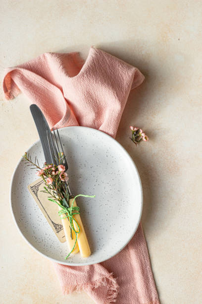 istock Romantic or spring table setting. Knife and fork, little pink flowers and linen napkin on a plate, light concrete background. Flat lay. 1311996409