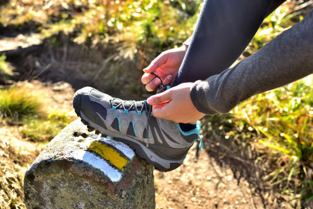 femme lissant ses chaussures de trekking sur une pierre de randonnée marquant la route touristique - lace one person vitality action photos et images de collection