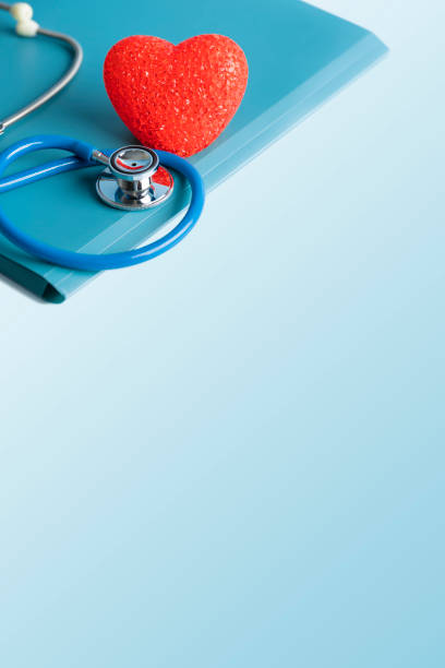A DSLR photo of a stethoscope with a red heart on a blue file. Blue gradient background, space for copy.