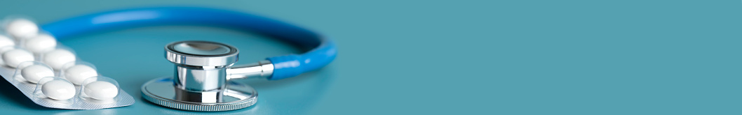 Close-up of a stethoscope with some pills blister on a blue background. Space for copy, shallow depth of field.