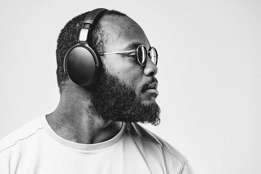 African-american ethnicity person at the studio with professional wireless black headphones is listening music. Concept for dj, pop, rap, r&b music photography.  Black and white photo with copy space