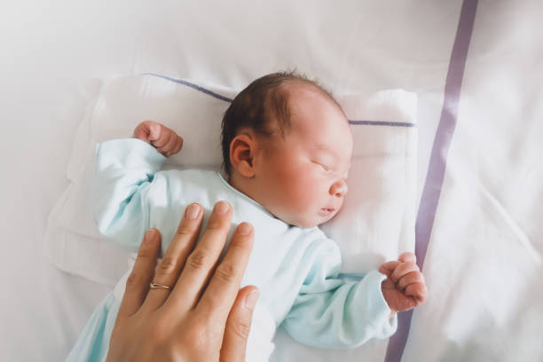 Mother and newborn resting after childbirth in maternity hospital room. Mother and newborn resting after childbirth in maternity hospital room. Mother hugging her sleeping newborn baby. baby bracelet stock pictures, royalty-free photos & images