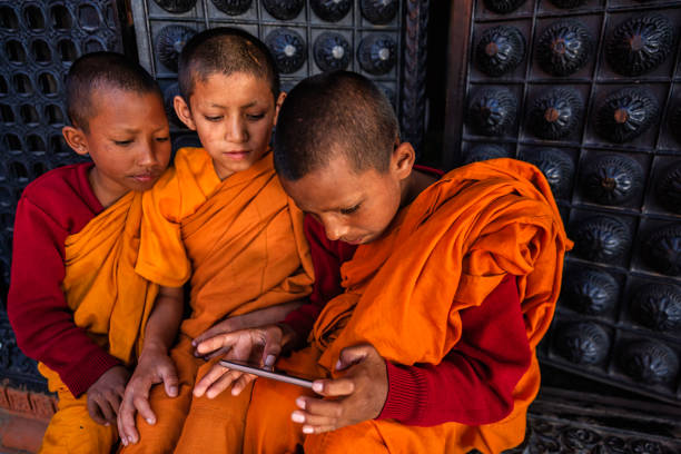 Novice Buddhist monks playing on mobile phone in the monastery in Bhaktapur, Nepal. Bhaktapur is an ancient Newar town in the east corner of the Kathmandu Valley, Nepal. It is the third largest city in Kathmandu valley and was once the capital of Nepal during the great Malla Kingdom until the second half of the 15th century. Bhaktapur is listed as a World Heritage by UNESCO for its rich culture, temples, and wood, metal and stone artwork.