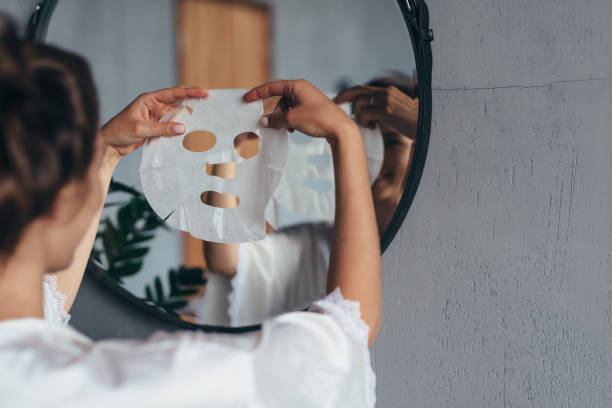 Woman with sheet mask in her hands in the bathroom before applying it to her face stock photo