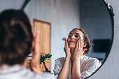 Woman applies foam to her face, cleansing her skin.