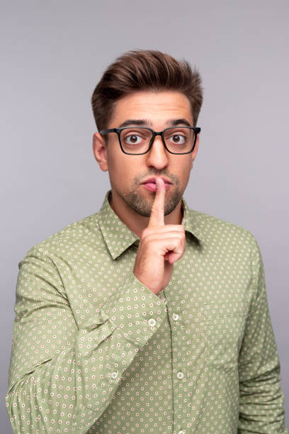 istock Young man telling secret and keeping forefinger on lips 1312022104
