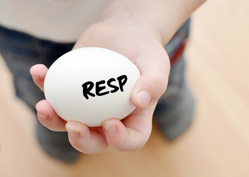 Closeup of a 3 year old boy holding an egg with RESP written on it symbolizing a Registered Education Savings Plan in Canada.