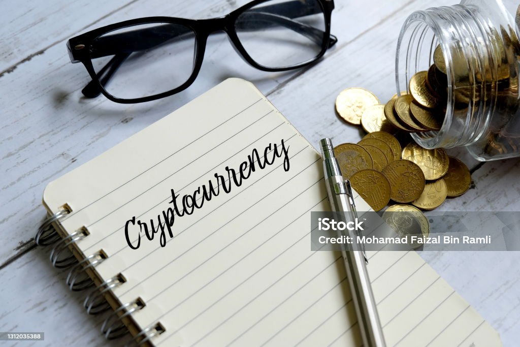 Sunglasses,jar of coins,pen and notebook written with 'CRYPTOCURRENCY' on white wooden background. Litecoin Stock Photo
