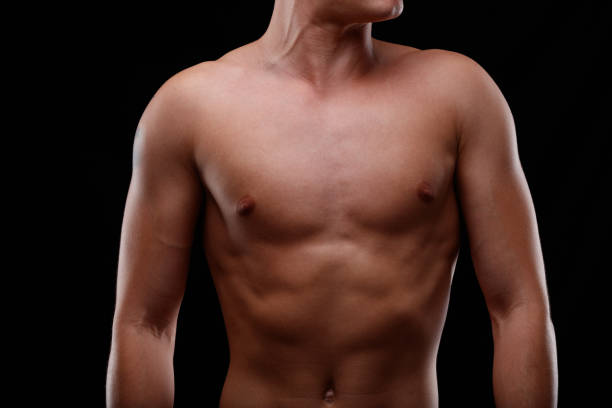 Front close up view of the bare chest of a young man Front close up view of the bare chest of an athletic toned young man over a black background man muscular chest stock pictures, royalty-free photos & images