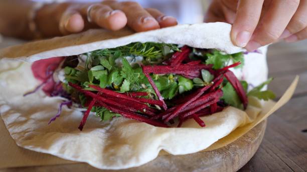 close up of hand wrapping pita for healthy vegan sandwich full of fresh vegetables. delicious plant based homemade recipes - asia cooked food gourmet imagens e fotografias de stock