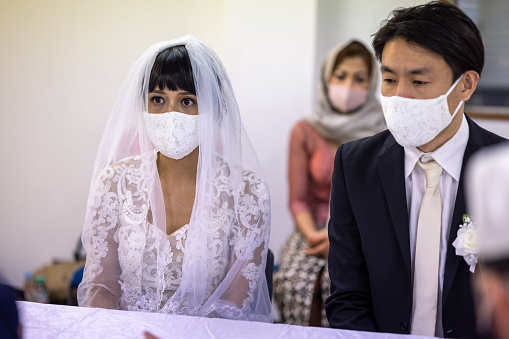 Indonesian woman and Japanese man having Islam style wedding ceremony and wedding party in Tokyo, Japan. Bride and groom, and participants are wearing face mask in most of the time to protect against coronavirus.