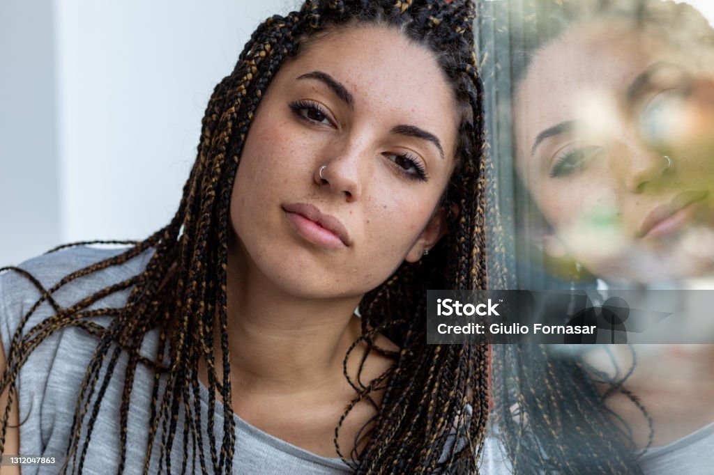 Young woman with dreadlocks and nose piercing Young woman with dreadlocks and nose piercing leaning against a window with reflection on the glass looking thoughtfully at the camera in close up Nose Ring Stock Photo