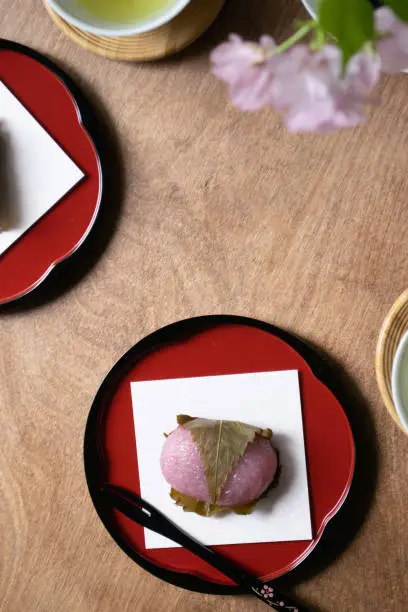 Japanese spring sweets, rice cakes filled with sweet bean paste and wrapped in a pickled cherry leaf, served on a wooden table with green tea.
