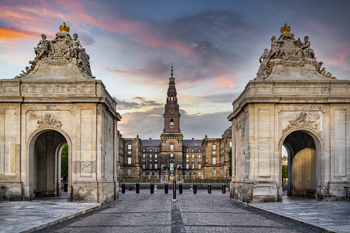 Christiansborg Palace Ridebane, Christiansborg Slot Main Entrance to the Royal Stables Street View with two Rococo Pavilions on each side of the Marble Bridge from the year 1739 under moody summer sunset twilight. Old Danish Parliament Tower - Christiansborg Palace Tower and in the background. Copenhagen, Denmark, Nordic Countries, Europe