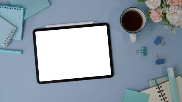 istock Top view of digital tablet with white screen, stylus pen, coffee cup and notebook on blue background. 1312050937
