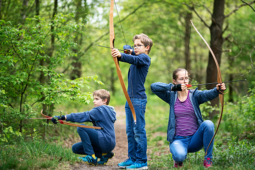 Three kids playing with bows in forest.\nNikon D850