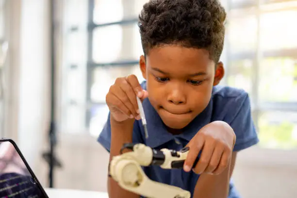 An african american boy use screwdriver setting robot kit.