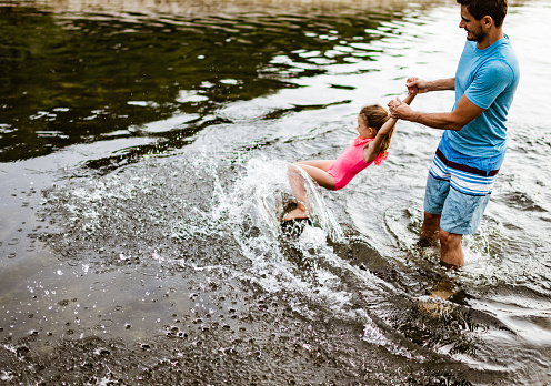 Single father and his daughter are having fun on a river during hot summer day.
