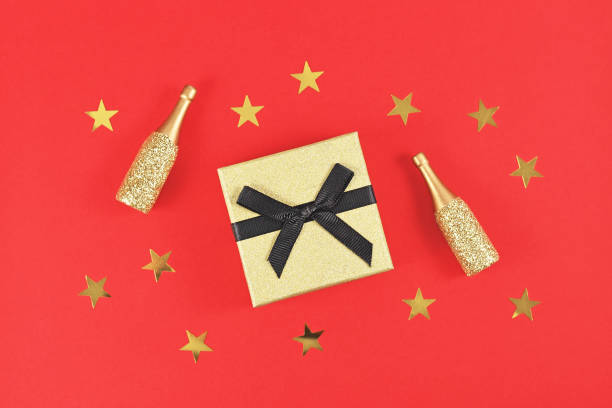 istock Golden gift box small Champagne bottles and stars on red background 1312058657