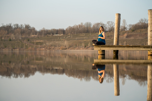 Happy pregnant woman relaxing on a jetty in nature