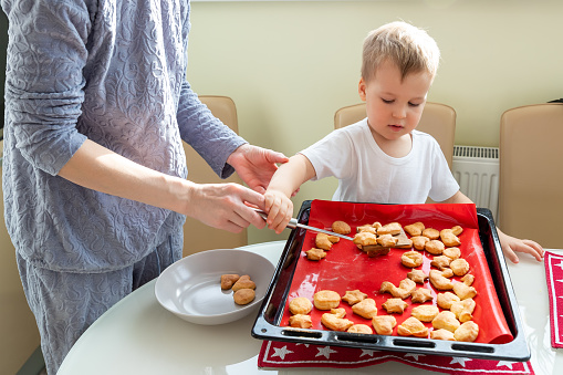 Young adult mother learn cooking sweet tasty cookies cute little toodler boy kid at home kitchen. Mom with small son baking sweet pastry homemade dessert. Parent child together activity.