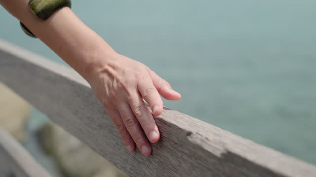 Close up woman hand touching and slide over wood bridge hand railing at sea in summer vacation