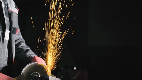 Forge workshop. Smithy manual production. Close up details of sparks, industrial worker using angle grinder and cutting steel. The blacksmith makes iron products for manufacture of fireplaces, stoves.