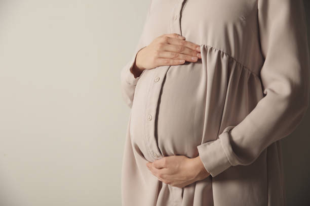 istock Pregnant woman touching her belly on light grey background, closeup. Space for text 1312076233