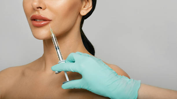 injection de remplissage de lèvres pour l’augmentation de la lèvre de la belle femme avec l’esthéticienne sur le fond gris. procédure d’augmentation des lèvres - big lips photos et images de collection