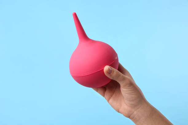 istock Woman holding pink enema on light blue background, closeup 1312083203