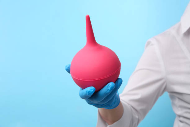 istock Doctor holding pink enema on light blue background, closeup 1312084003