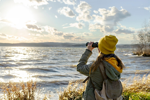 Young woman looking through binoculars at birds on the lake. Birdwatching, zoology, ecology. Research in nature, observation of animals. Ornithology