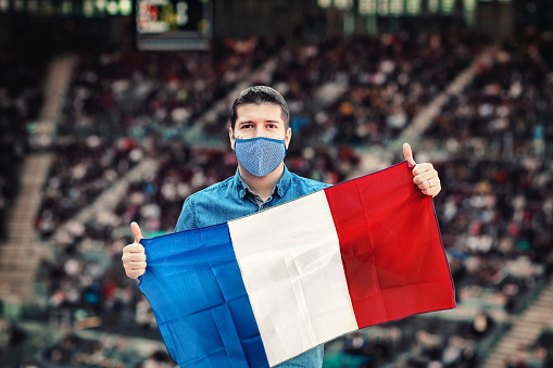 Happy football fan with face mask holding national flag of France cheering his favorite soccer team at international sport event at stadium – Young supporter with painted face having fun at Euro cup