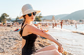 A woman in a swimsuit sits on the beach and scratches her hand with redness and a rash. Outdoor. Concept of insect bites and allergies