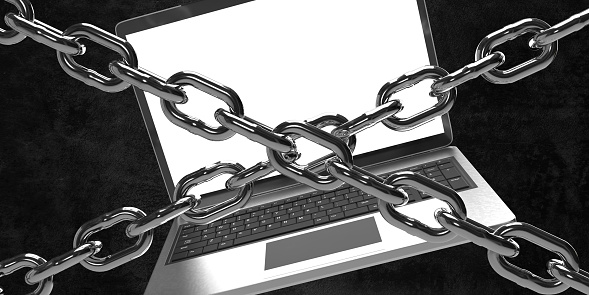 Digital detox or Computer security concepts: Laptop computer behind steel chains. Black background and limited copy space on empty laptop screen.