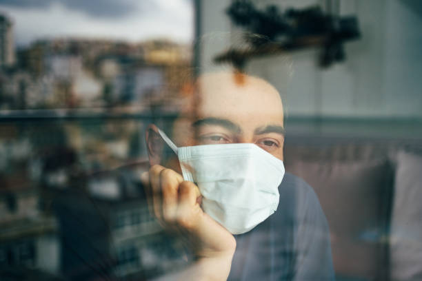 istock Man in quarantine wearing a mask and looking through the window 1312093405