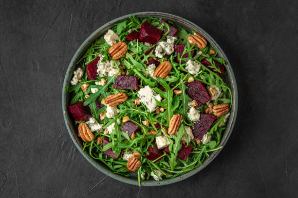 istock Beet or beetroot salad with fresh arugula, blue cheese and pecan nuts in a plate on black background. top view 1312094975