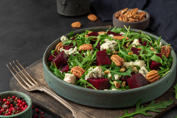 istock Salad with fresh arugula, beetroot, gorgonzola cheese and pecan nuts in a plate with fork on black background. vegetarian food 1312095000