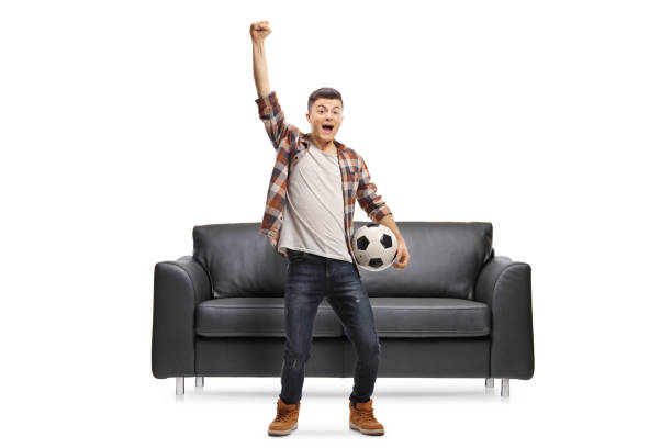 istock Guy jumping in front of a sofa, holding a football and shouting 1312096529
