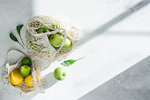 Bright green and yellow fruits in mesh cotton bags on white sunny background