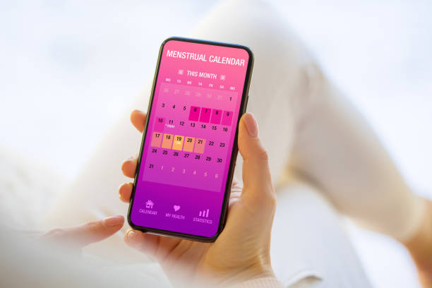 woman tracking periods by using menstrual calendar app on phone - ovulação imagens e fotografias de stock