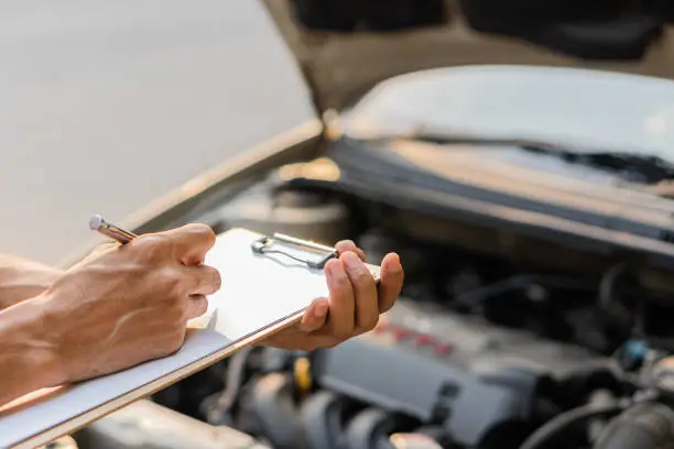 Photo of The auto mechanic checks the car engine with the check written in the car service engine repair checklist notebook.