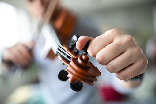 Young male violinist tuning the strings before playing violin at home