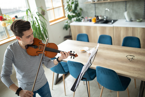 Young man enjoying playing violin at home