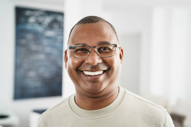 hombre africano feliz mirando la cámara en el interior de casa - concéntrate en la cara - senior adult african descent men african ethnicity fotografías e imágenes de stock