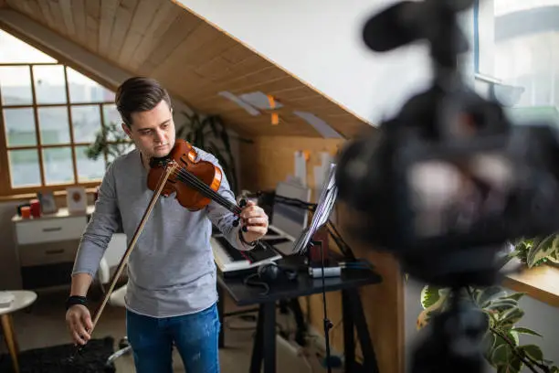 Photo of Young man recording violin class tutorial using video camera at home