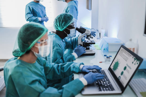 istock Medical workers in hazmat suit working with microscope and laptop computer inside modern laboratory hospital - Focus on microscope 1312110037