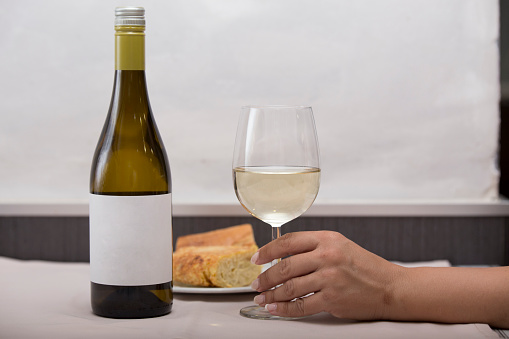 A person holding a glass of white wineA person holding a glass of white wine with food in the background on a restaurant table. Drink and food concept